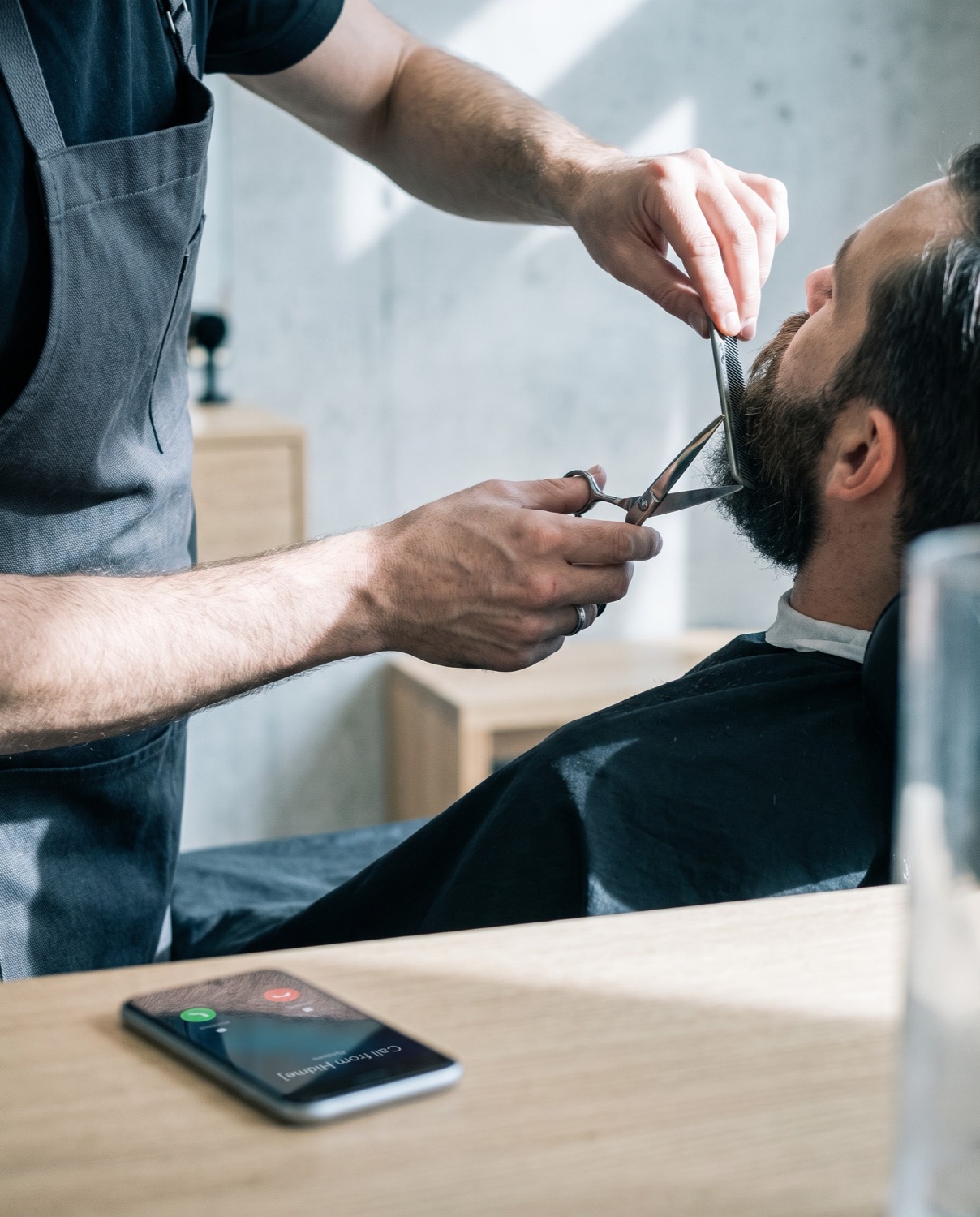 Un barbier taille une barbe aux ciseaux pendant que son téléphone sonne sur le comptoir.